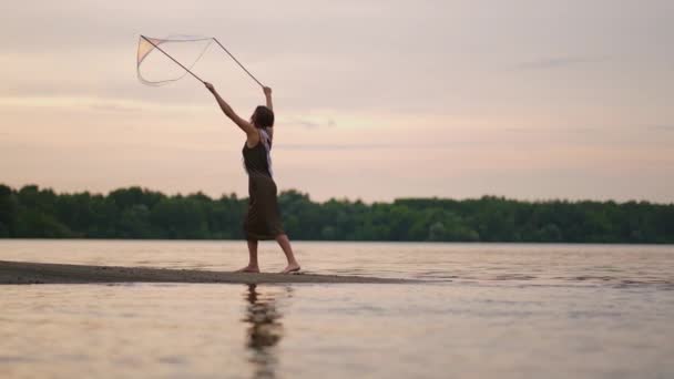 Una joven artista muestra un espectáculo de burbujas de jabón haciendo estallar enormes burbujas de jabón en la orilla de un lago al atardecer. Mostrar un hermoso espectáculo de burbujas de jabón en cámara lenta — Vídeos de Stock