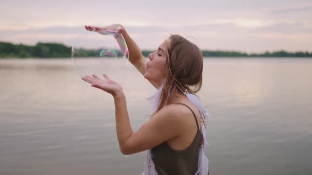 Egy fiatal lány művész szappanbuborékokkal varázsolja a trükköket. Hozzon létre szappanbuborékok a kezében, és felfújja őket helyét színpadi cirkusz show naplementekor — Stock videók
