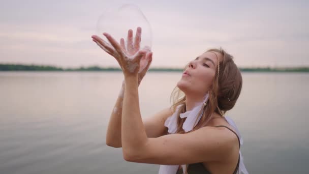 Egy fiatal lány művész szappanbuborékokkal varázsolja a trükköket. Hozzon létre szappanbuborékok a kezében, és felfújja őket helyét színpadi cirkusz show naplementekor — Stock videók
