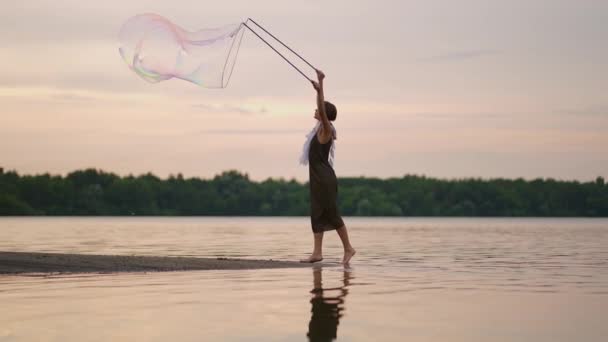 En ung flicka konstnär visar magiska trick med hjälp av enorma såpbubblor. Skapa såpbubblor med hjälp av pinnar och rep vid solnedgången för att visa en teatralisk cirkus show — Stockvideo
