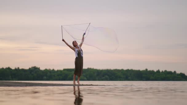 En ung flicka konstnär visar magiska trick med hjälp av enorma såpbubblor. Skapa såpbubblor med hjälp av pinnar och rep vid solnedgången för att visa en teatralisk cirkus show — Stockvideo