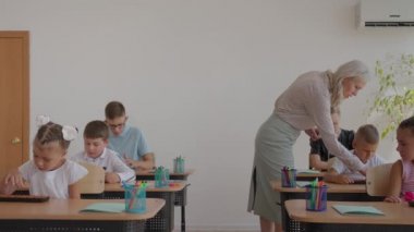 Sınıftaki çocuklar masalarında oturuyorlar ve öğretmen sınıfın etrafında yürüyor ve dersin konusunu açıklıyor. Akıllı Çocuklar Arkadaş Canlısı Modern Çevrede Öğreniyor