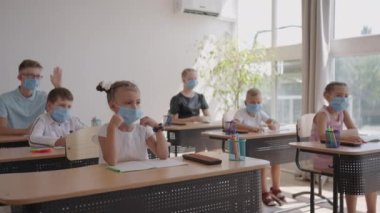 Öğretmenlerin sorularına cevap vermek için elinizi kaldırın. COVID-19 salgını sırasında okulda yüz maskesi takan çok ırklı çocuklar..