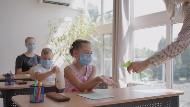 Die Lehrerin behandelt vor dem Unterricht die Hände eines antiseptischen Mädchens im Klassenzimmer. Coronavirus und die Pandemie in der Schule. Die Arbeit der Schule im epidemischen Modus — Stockvideo