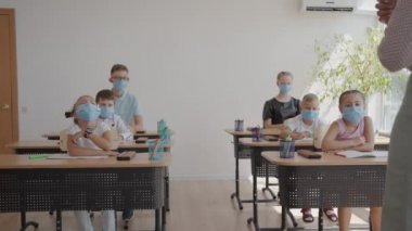 Öğretmenlerin sorularına cevap vermek için elinizi kaldırın. COVID-19 salgını sırasında okulda yüz maskesi takan çok ırklı çocuklar..