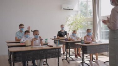 Öğretmenlerin sorularına cevap vermek için elinizi kaldırın. COVID-19 salgını sırasında okulda yüz maskesi takan çok ırklı çocuklar..