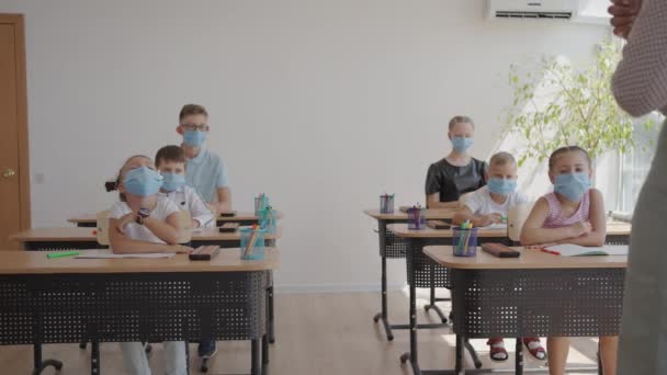 Levanta la mano para responder a la pregunta de los profesores. Grupo multiétnico de niños con máscaras faciales en la escuela durante la pandemia de COVID-19. — Vídeos de Stock