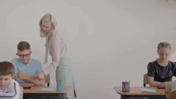 Lehrerin steuert Lernprozess in der Grundschule. Eine Lehrerin geht zwischen den Schreibtischen hin und her und kümmert sich um die Bearbeitung der Aufgabe — Stockvideo