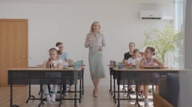 İlkokulda kadın öğretmen öğrenme sürecini kontrol ediyor. Bir bayan öğretmen masaların arasında yürür ve görevin tamamlanmasıyla ilgilenir.
