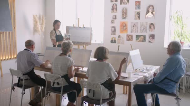 Hög vinkel syn på glada äldre vänner målning på duk. En äldre kvinna ler medan hon ritar med gruppen. Seniorer deltar målning klass tillsammans. Senior män som har kul målning i konstklassen — Stockvideo