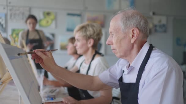 Vista de ángulo alto de alegres amigos mayores pintando sobre lienzo. Mujer mayor sonriendo mientras dibuja con el grupo. Personas mayores que asisten a clases de pintura juntas. Hombres mayores que se divierten pintando en clase de arte — Vídeos de Stock