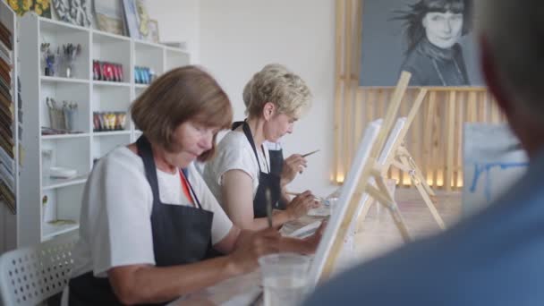 O professor mostra um grupo de amigos de aposentados em idosos em cursos de desenho. Um grupo de homens e mulheres idosos se reúnem e sorriem — Vídeo de Stock