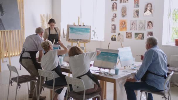 Vista de alto ângulo de amigos seniores alegres pintando sobre tela. Mulher sênior sorrindo enquanto desenha com o grupo. Idosos que frequentam a aula de pintura juntos. Sénior homens se divertindo pintura na aula de arte — Vídeo de Stock