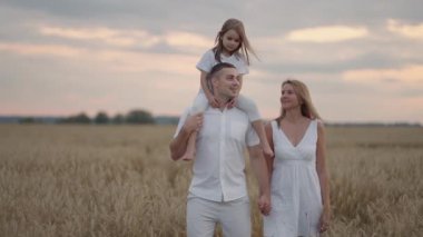Kızlarla el ele tutuşan ve gün batımında buğday tarlasında koşan iki genç ebeveyn. Arpa çayırlarında koşan ve doğanın tadını çıkaran mutlu bir aile. Yavaş çekim