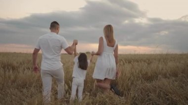 Mutlu gülümseyen aile gün batımında altın tarlada el ele yürüyor. Mutlu bir aile çayırda yürüyor ve oynuyor.