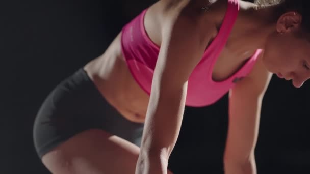 Fit mixed race female athlete on a running track at an outdoor sports stadium starting a race from starting blocks, in slow motion backlit with lens flare. Night — ストック動画