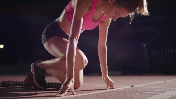 Female athlete training at running track in the dark stadium. Slow motion. A young female athlete gets into the pads and starts in the race. close-up of a girl runner — kuvapankkivideo