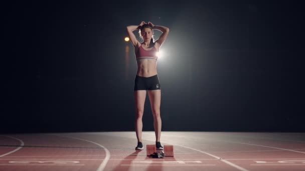 Vrouwelijke atleten warmen zich op bij het hardlopen voor een race. In slow motion. Vrouwelijke loper op atletiekbaan hurkend bij de startblokken voor een race. — Stockvideo