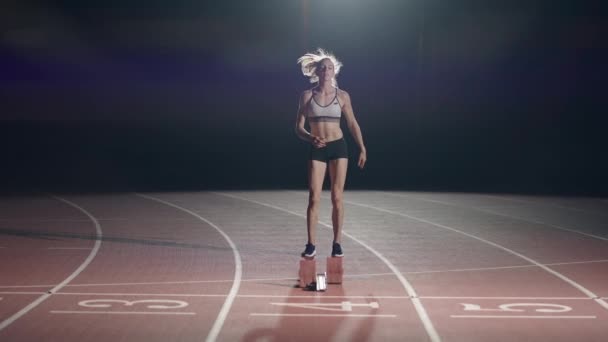 Las atletas femeninas se calientan en la pista antes de una carrera. En cámara lenta. Mujer corredora en pista de atletismo agachándose en los bloques de salida antes de una carrera. — Vídeos de Stock