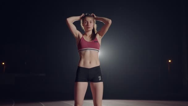 Las atletas femeninas se calientan en la pista antes de una carrera. En cámara lenta. Mujer corredora en pista de atletismo agachándose en los bloques de salida antes de una carrera. — Vídeos de Stock