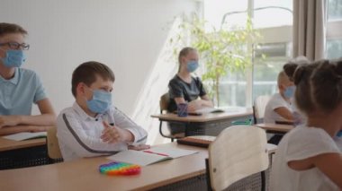 Öğretmenlerin sorularına cevap vermek için elinizi kaldırın. COVID-19 salgını sırasında okulda yüz maskesi takan çok ırklı çocuklar..