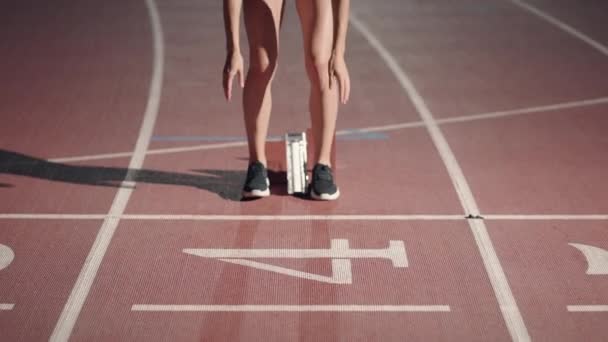 Vista frontal de una atleta que comienza su carrera en una pista de atletismo. Corredor despegando de los bloques de partida en pista de atletismo. Cámara de zoom. Movimiento lento — Vídeo de stock