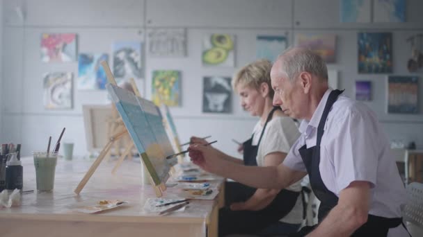 Повільний рух Старі люди відвідують курси малювання. Вчитель допомагає пенсіонерам, які відвідують курси малювання. Група друзів у відставці на уроці малювання — стокове відео