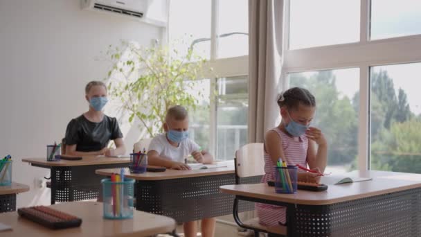 Schulkinder sitzen im Klassenzimmer und heben die Hände, um in Zeitlupe die Fragen der Lehrer in Schutzmasken zu beantworten — Stockvideo
