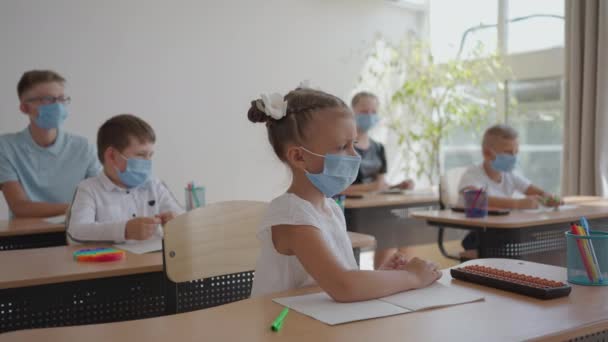 Barn i skolan sitta i klassrummet och lyfta händerna svara lärarna frågor i skyddande masker i slow motion — Stockvideo