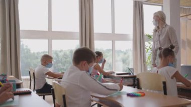 Okulda, sınıfta, çocuklar koruyucu maskelerle not defterlerine yazarlar, sosyal mesafeyi gözlemlerler. Salgın sırasında okul eğitimi