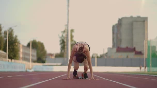 Caucasian young brunette woman shit for a run in the stadium comes up to the running sides and starts the sprint race in slow motion — Vídeo de Stock