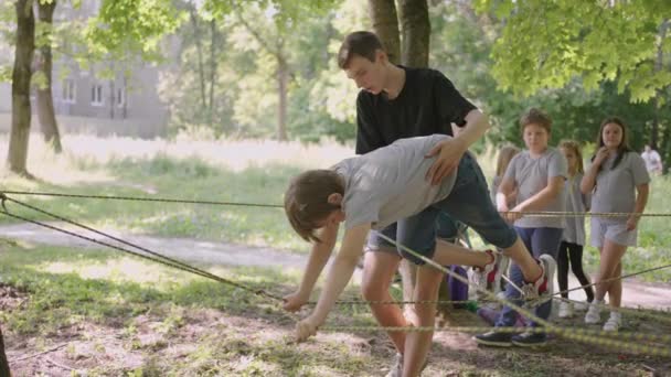 Chłopiec uczy się chodzić po kolejkach linowych i pokonywać klify i przeprawy linowe w obozie letnim. — Wideo stockowe