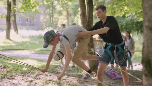Kinder auf einer Sommerlagerwanderung bewegen sich mit Hilfe eines Führers, der Kindern Klettern und Tourismus beibringt, entlang der Seile. Junge im Wald überwindet Seilbarriere — Stockvideo