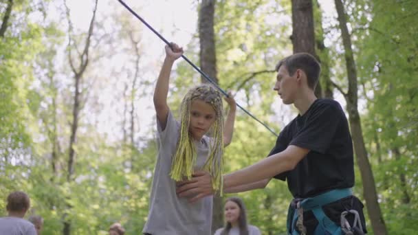 サマーキャンプでは、娘がロープの障害物やロッククライミングを克服することを学びます。観光やハイキングについて子供たちに教える — ストック動画