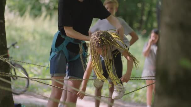 En el campamento de verano, mi hija aprende a superar obstáculos de cuerda y escalada en roca. Enseñar a los niños sobre el turismo y el senderismo — Vídeos de Stock