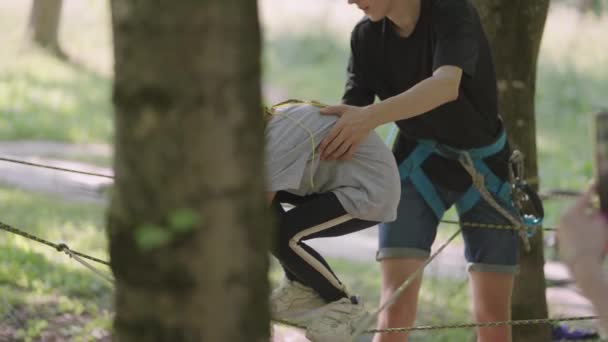 Unerschrocken klettert ein aktives Kind auf den Seilen zwischen den Bäumen. Mädchen in einem Abenteuerpark passieren Hindernisse auf der Seilbahn. Kinderlager, Sommerlager, — Stockvideo