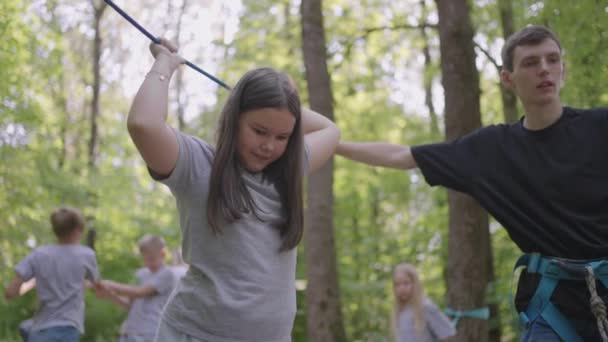 No acampamento de verão, minha filha aprende a superar obstáculos de corda e escalada. Ensinar as crianças sobre turismo e caminhadas — Vídeo de Stock