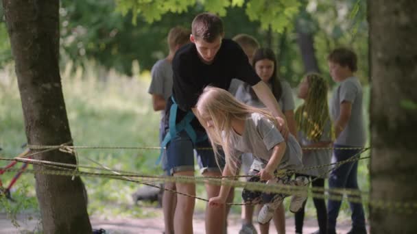 No acampamento de verão, minha filha aprende a superar obstáculos de corda e escalada. Ensinar as crianças sobre turismo e caminhadas — Vídeo de Stock