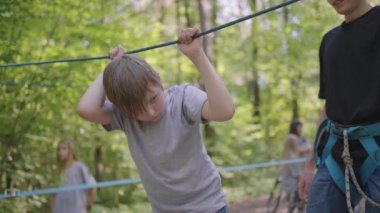 Yaz kampında yürüyüş yapan çocuklar, çocuklara kaya tırmanışı ve turizm öğreten bir rehberin yardımıyla ipler boyunca ilerliyorlar. Ormandaki bir çocuk halat engelini aştı.