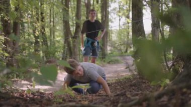 Yaz kampında yürüyüş yapan bir çocuk yerde sürünerek ve yuvarlanarak engelleri aşıyor. Eğlenceli çocuklar zorluklar