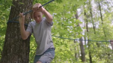 İp parkında tırmanma ekipmanı içinde küçük bir çocuk. Bir grup beyaz çocuk acemi birliğinde eğitim görüyor. Çocuk kampında, çocuklara engelleri aşmaları öğretilir. Bir halat geçidinin yardımıyla.