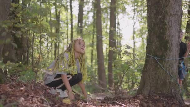 Crianças em um acampamento de verão caminhadas rasteja no chão. Treinamento de passar obstáculos rastejando no chão. Uma menina cai na floresta em uma missão de acampamento — Vídeo de Stock