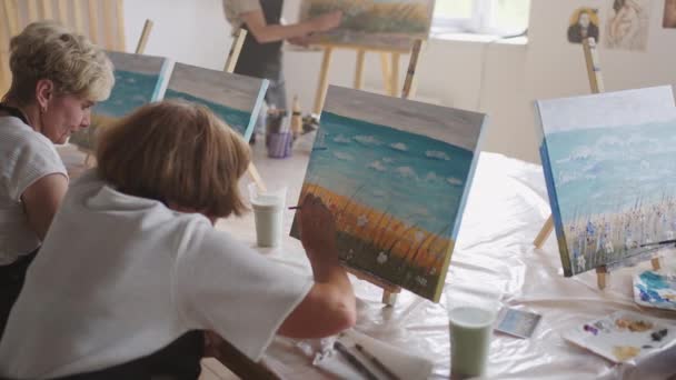 En gammal pensionerad kvinna målar en bild tillsammans med vänner. En äldre grupp vänner och en äldre kvinna ritar bilder tillsammans. — Stockvideo