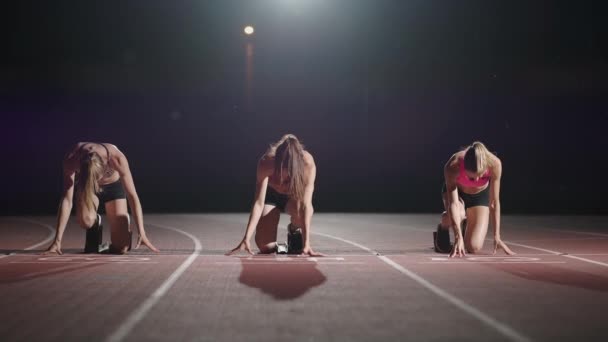 Vista frontal zoom cámara tres mujeres en el estadio por la noche en cámara lenta iniciar y ejecutar a la cámara — Vídeo de stock