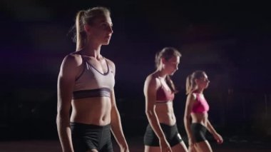 Spor kıyafetleri içinde koşan genç ve güzel kadınlar ve spor ayakkabıları koşu pistinde birlikte yarışmaya hazırlanıyorlar. Çizgiden başla ve yarışa karanlıkta ağır çekimde başla.