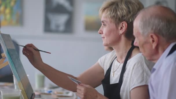 Een oude gepensioneerde vrouw schetst samen met vrienden een beeld. Een oudere groep vrienden en een oudere vrouw tekenen samen foto 's.. — Stockvideo