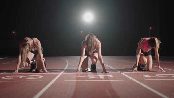 Vista frontal zoom cámara tres mujeres en el estadio por la noche en cámara lenta iniciar y ejecutar a la cámara — Vídeos de Stock