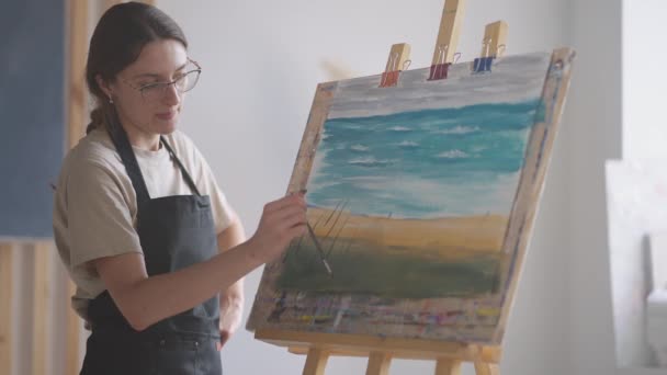 Joven profesora de pintura demuestra la técnica de aplicar pintura acrílica sobre lienzo — Vídeo de stock