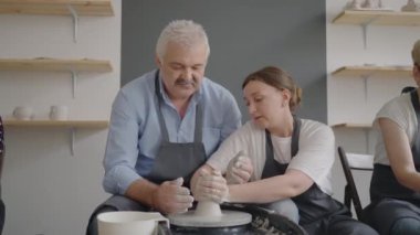 Kadın bir usta, yaşlılara ders veren kıdemli bir adamla yeteneklerini paylaşıyor. Büyükbabaya seramik kil ile çömlekçi çarkı üzerinde çalışma tekniğini göster.