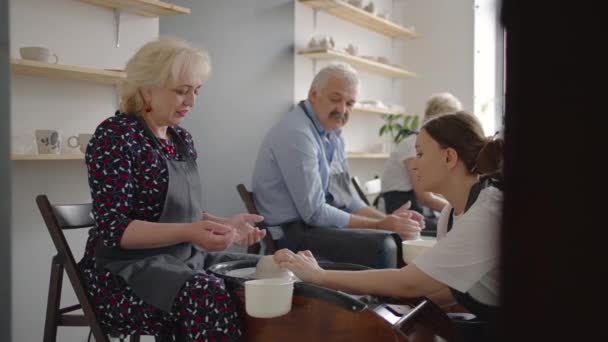 A young woman teaches a group of senior women and a man of 60-70 years old to pottery. Activities for the elderly — Stock Video